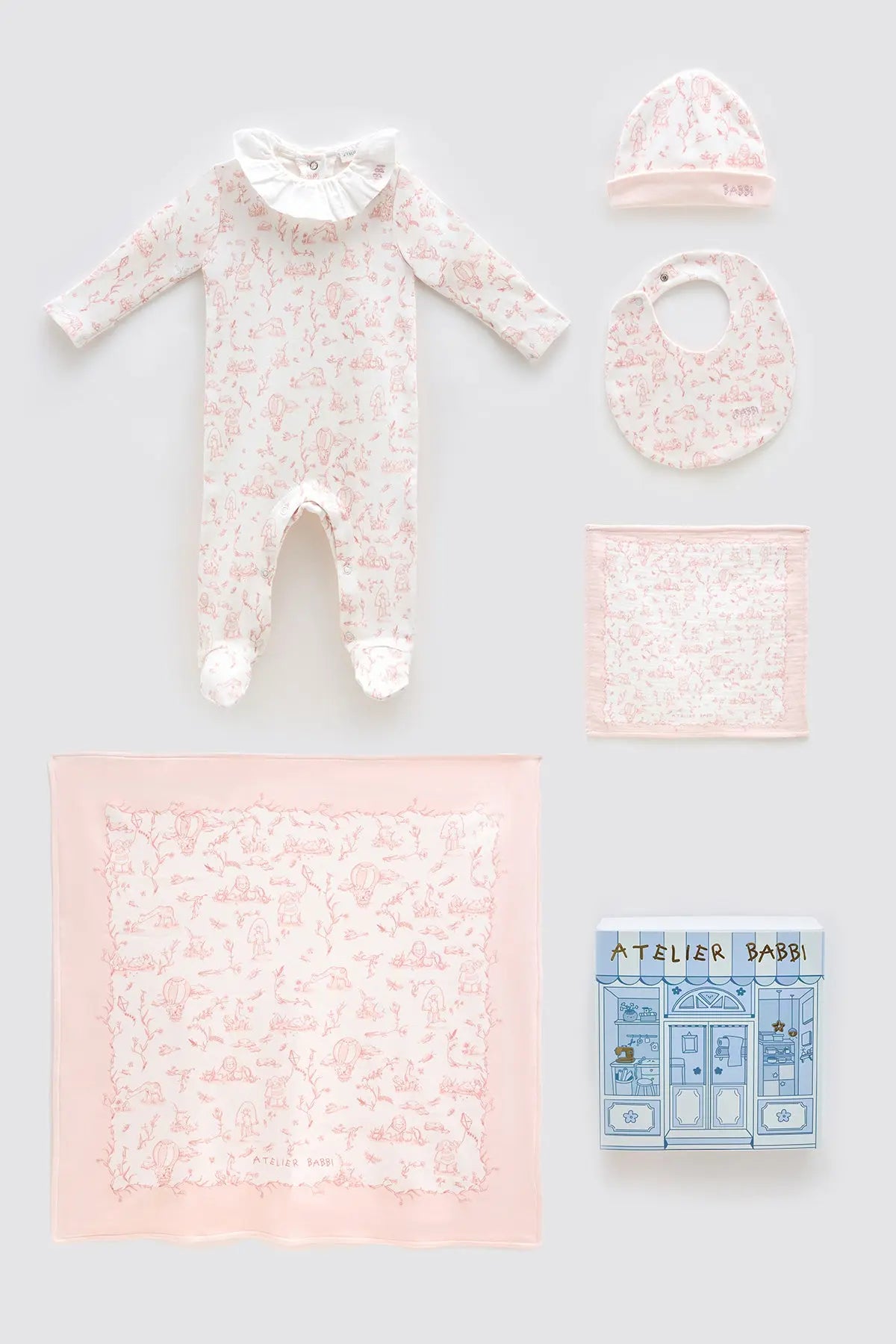 Atelier Babbi Toile de Jouy Pink 5-piece newborn gift set featuring a soft pink printed romper with ruffled collar, baby hat, bib, multi-use cloth, and muslin blanket — beautifully arranged with pastel packaging, crafted from 100% organic cotton.