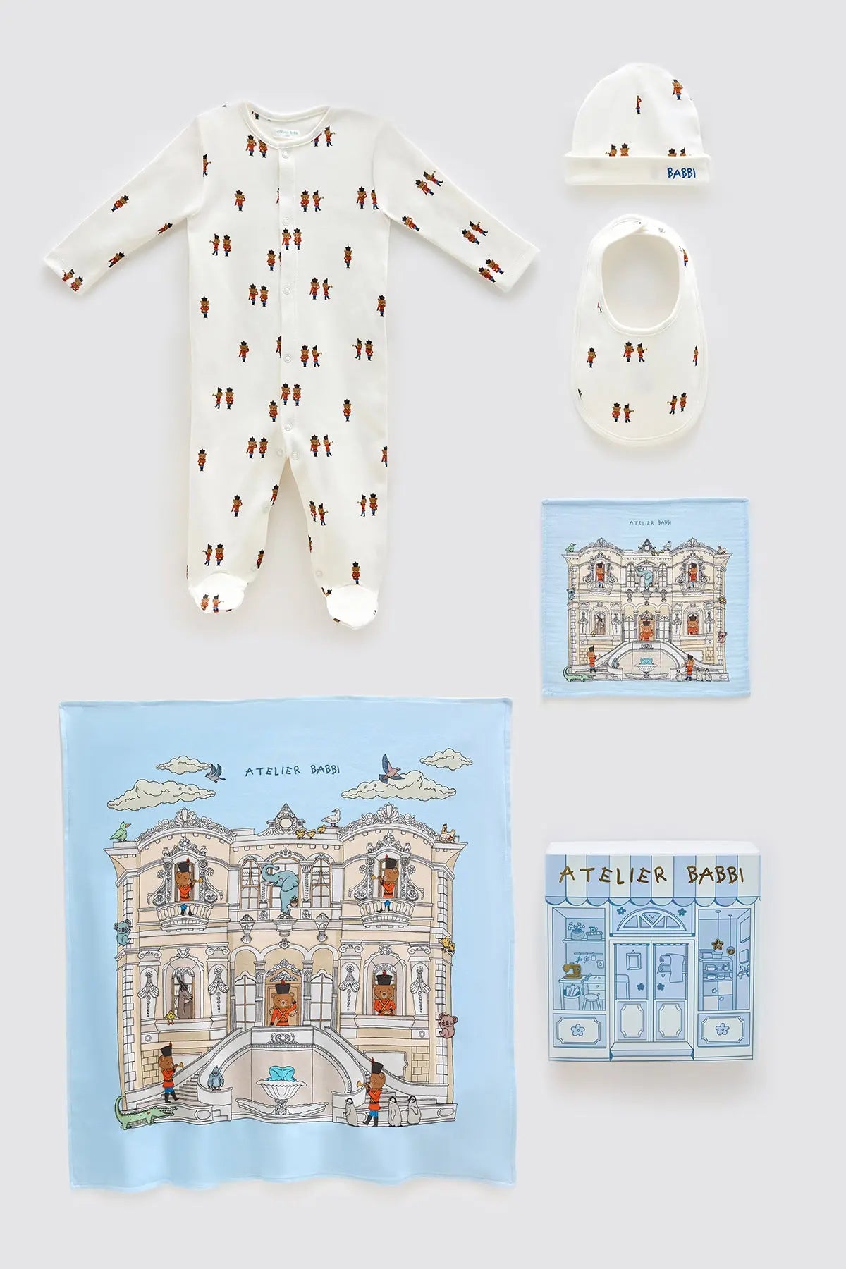 5-piece newborn gift set featuring the Tin Soldier theme, with a romper, hat, bib, muslin cloth, and illustrated satin blanket, inspired by a whimsical royal palace design in soft blue tones.