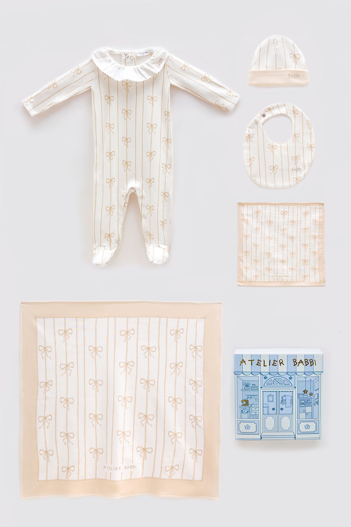 Beige Ribbon newborn gift set including a footed romper with frill collar, matching hat, bib, muslin burp cloth, and large muslin blanket, all featuring elegant beige bow patterns, styled with Atelier Babbi gift box.