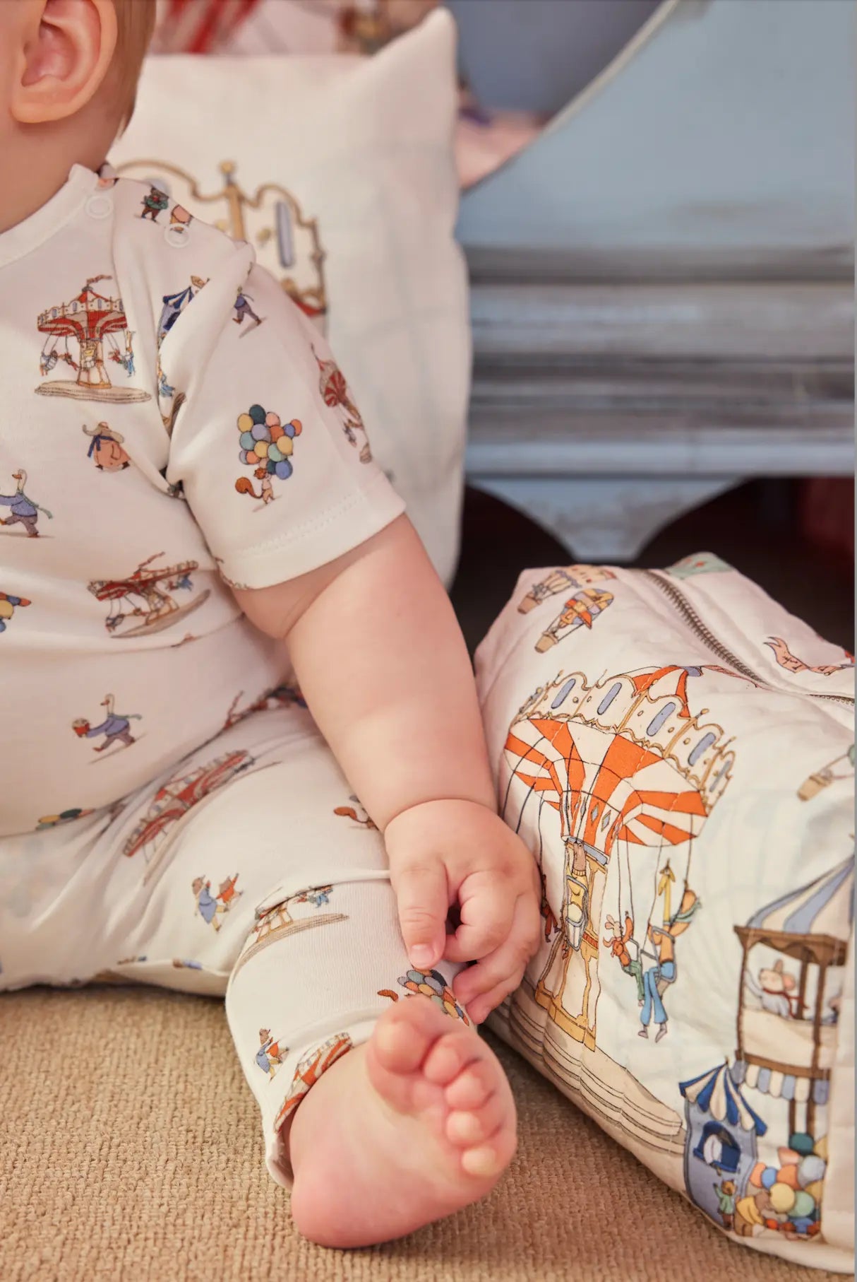 Baby wearing Funfair collection outfit sitting next to Funfair diaper pouch with carnival print.