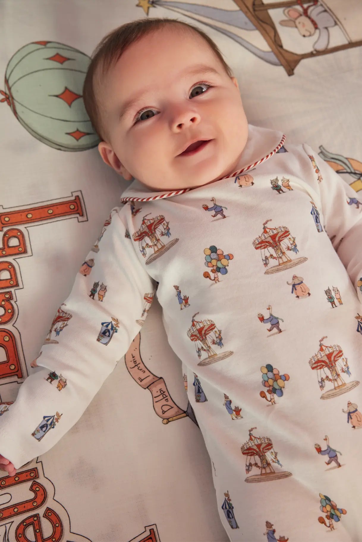 Baby wearing a patterned onesie lying on a decorative blanket with colorful designs.