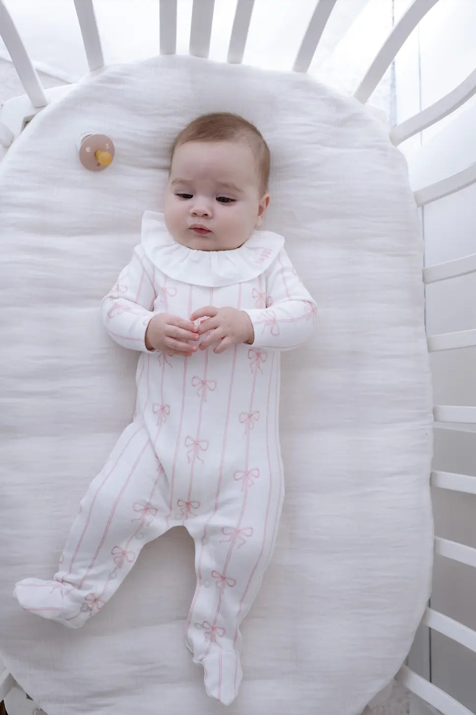 Organic pink ribbon baby footed onesie laid flat on a soft blanket