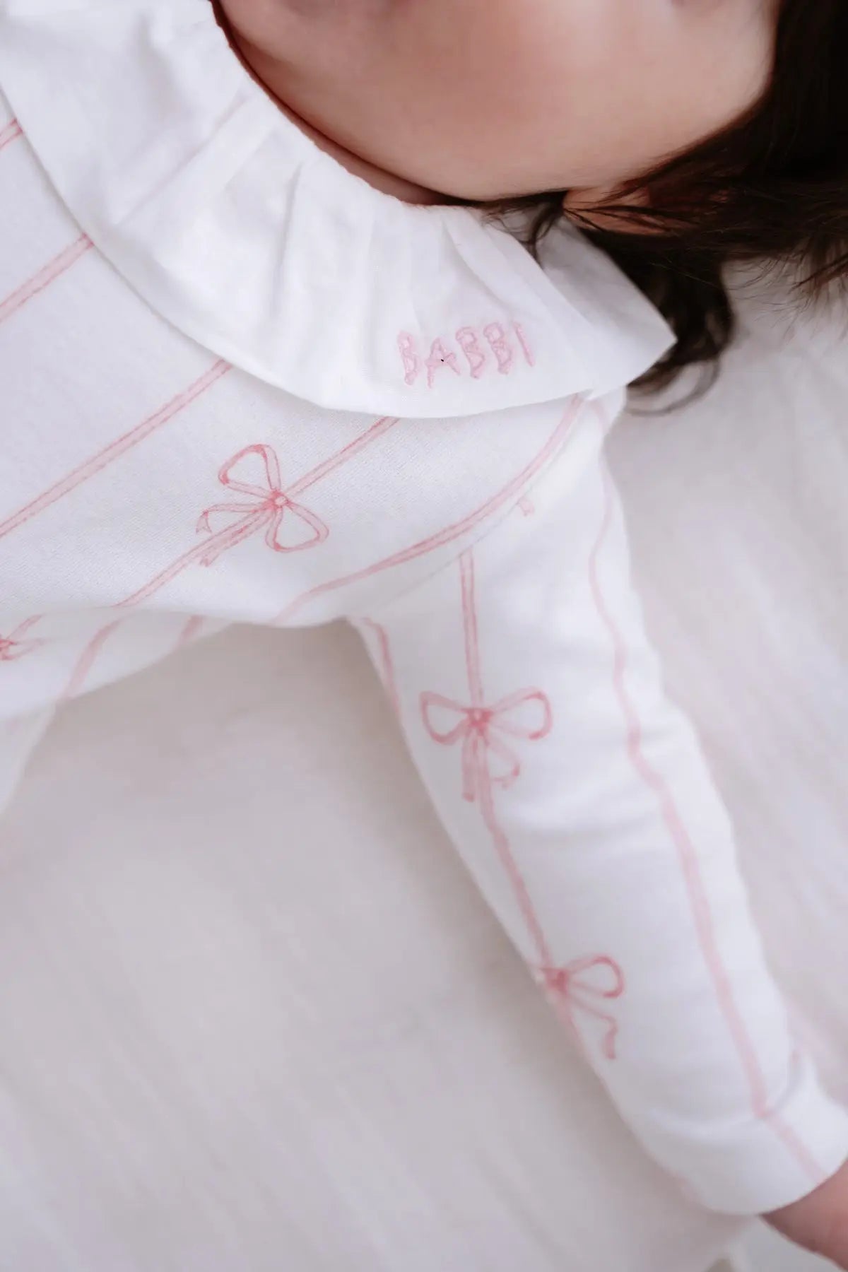 Cozy baby onesie in soft pink ribbon design on neutral background
