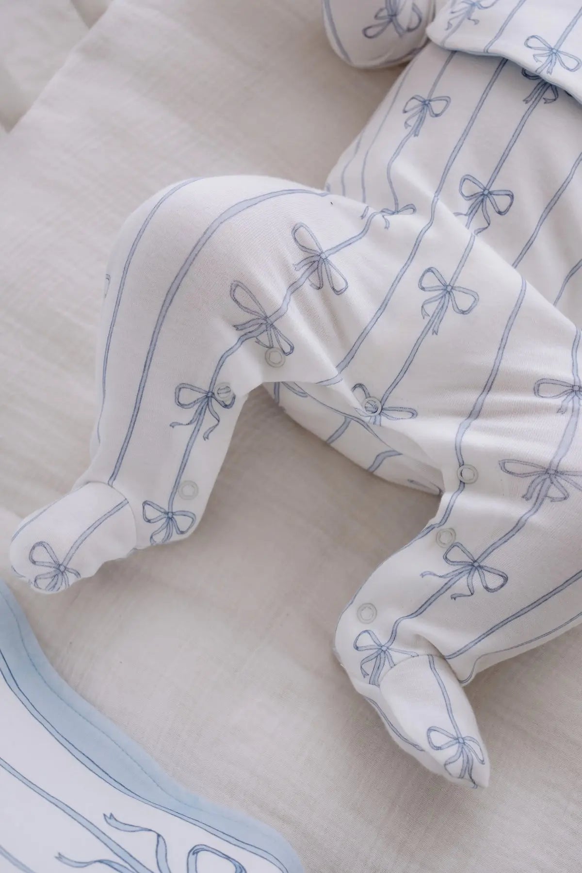 Close-up of a baby wearing a soft footed jumpsuit from Atelier Babbi’s Blue Ribbon collection, showcasing delicate bow patterns on white organic cotton fabric.