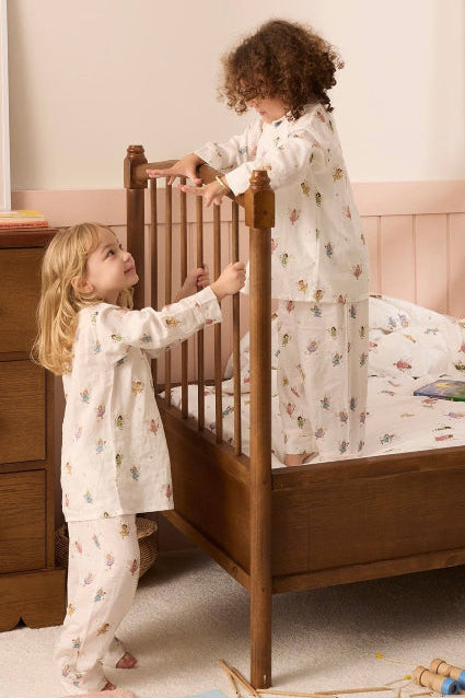 Two children in matching pajamas standing by a wooden bed in a bedroom.